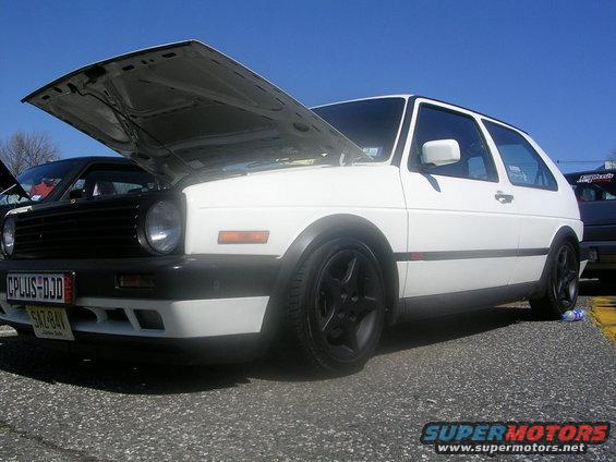 White Volkswagen Golf Mk2 with hood open, black wheels, and aftermarket front bumper