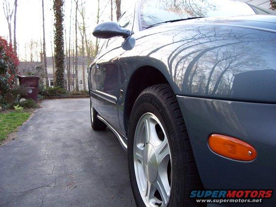 Side view of a dark blue sedan parked on a driveway. Trees and a house are in the background