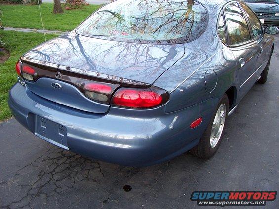 1999 Ford Taurus rear quarter panel and taillights, parked on driveway. Another car is visible in the background
