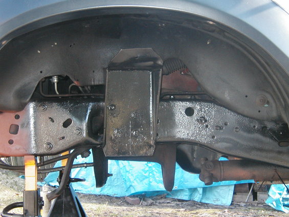close-up of vehicle frame and suspension parts, with a blue tarp underneath