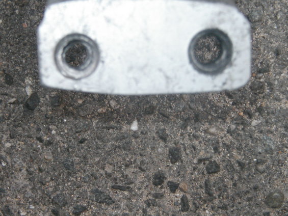Metal bracket with two circular bolt holes against asphalt