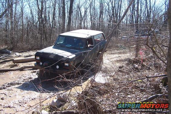 Dark SUV navigating a muddy, wooded trail with logs and branches