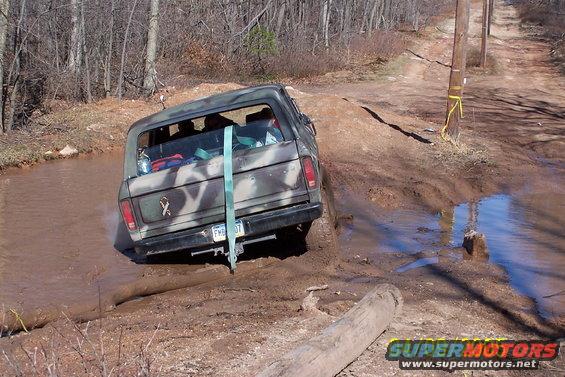 1979 Ford Bronco in camouflage driving through mud on a dirt road