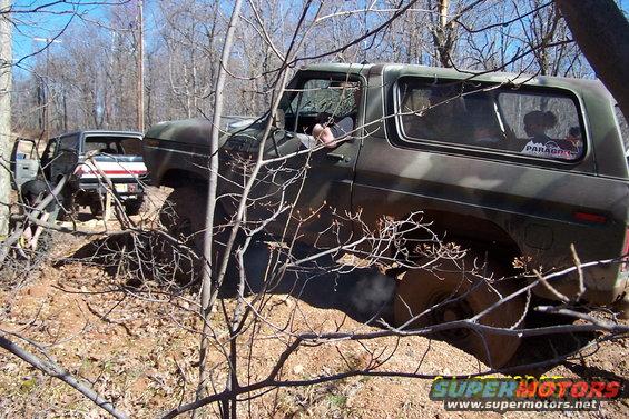 Camouflage 1979 Ford Bronco navigating rough terrain with another vehicle behind