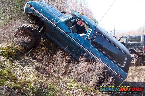 Blue 1978 Ford Bronco tilted on a hill with large tires, showing its side and interior
