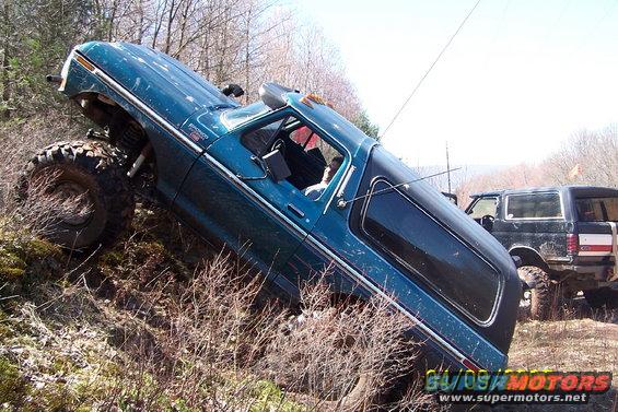 Teal 1979 Ford Bronco tilted on a hill, with another SUV behind it