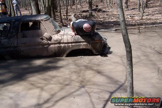 Mud-covered 1970s truck stuck in muddy water, a man is on its hood