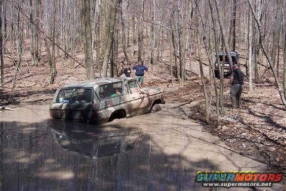 Camouflaged 1979 Ford Bronco stuck in mud pit, rear view