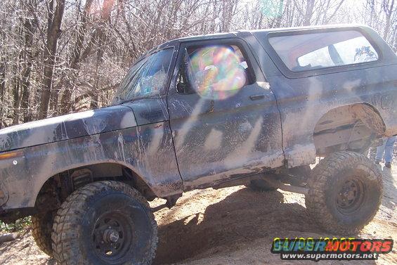 Mud-covered dark green 1978 Ford Bronco off-roading, viewed from the front-left