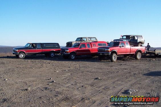 Several pickup trucks and an SUV parked on a dirt lot under a clear blue sky