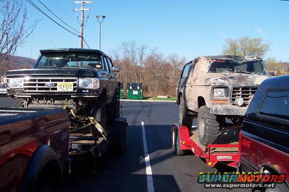 Mud-covered 1978 Ford Bronco on a red trailer next to a black Ford truck on a black trailer