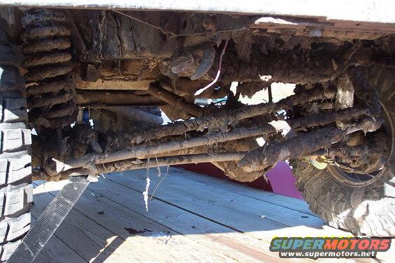 Mud-caked front suspension and steering linkage of a vehicle, with a tire visible on the right