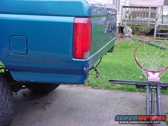 Blue pickup truck bed with rust streaks and a damaged taillight. Exposed wiring hangs near the rear bumper