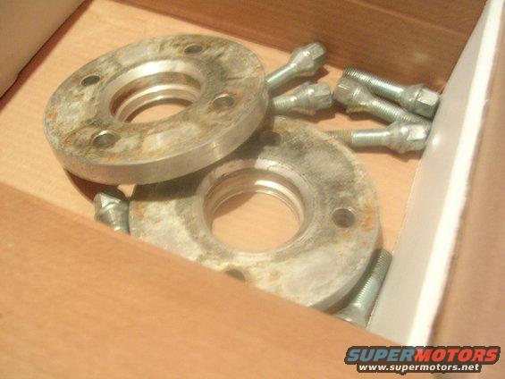 Two metal wheel spacers and several lug bolts are in a box