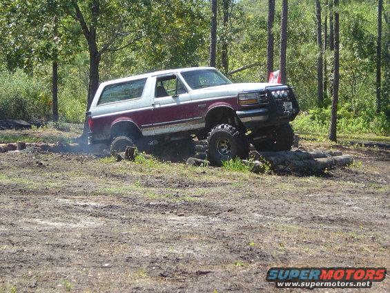 Maroon and white 1993 Ford Bronco off-roading over logs
