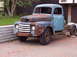 1948 Mercury M 100 - A heavily rusted 1948 Mercury M 100 truck sits in a driveway, showing significant wear and missing body panels.
