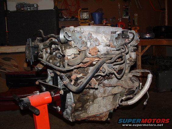 Engine assembly on an orange engine stand, showing hoses and intake manifold