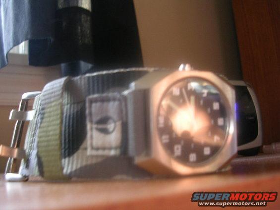 Watch with camouflage strap and silver case, resting on a wooden surface