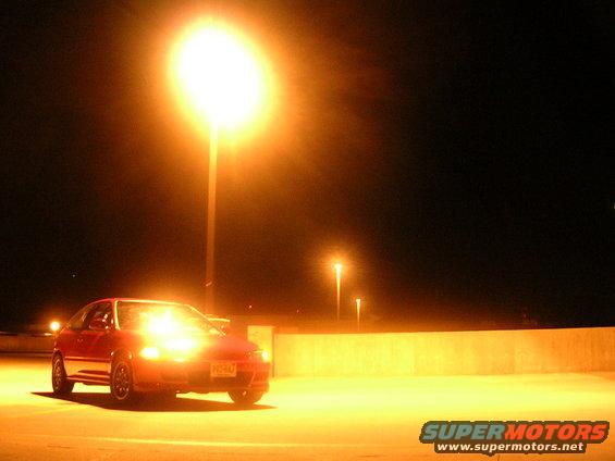Red hatchback parked under a bright street light at night