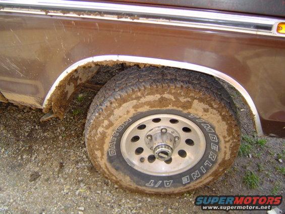 Brown vehicle's muddy wheel and fender with chrome trim. Tire has 'Dayton Timberline A/T' text