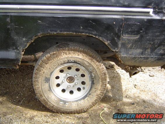 Close-up of a muddy rear wheel and rusted wheel well on a black truck
