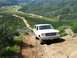 1988 Ford Bronco - A white 1988 Ford Bronco navigates a winding dirt road in a hilly, green landscape, with several other vehicles following.