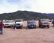 1988 Ford Bronco - Several Ford Broncos and F-Series trucks are parked on a dirt lot with hills in the background.