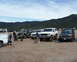 1988 Ford Bronco - A group of off-road vehicles are gathered in a dusty lot with a mountainous landscape under a cloudy sky.