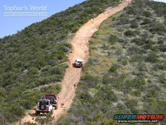 three off-road vehicles climbing a steep dirt trail on a hillside