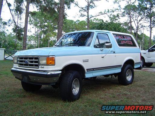 Two-tone blue and white Ford Bronco with aftermarket wheels, parked on grass