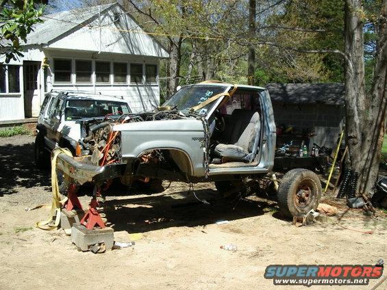 Disassembled pickup truck on jack stands, another SUV behind it