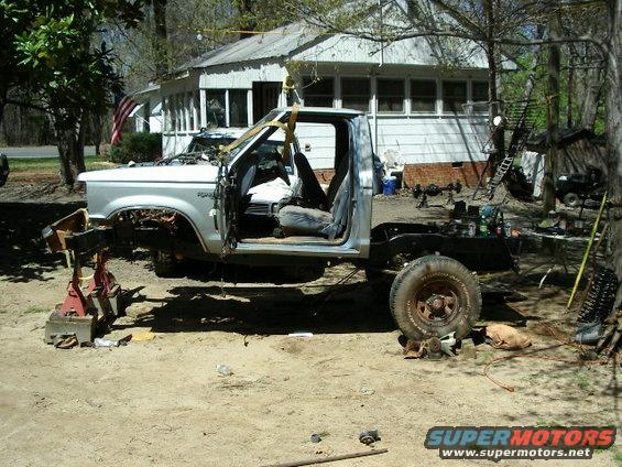 Ford pickup truck body lifted off frame with engine exposed, parked outside a house