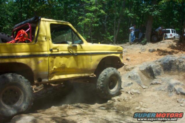 Yellow off-road SUV with roll cage and large tires navigating rocky terrain