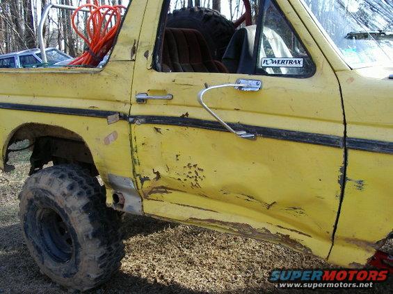 Yellow 1985 Ford Bronco side view with dented door and off-road tires