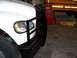 1978 Ford F-250 - A white truck's front corner is visible, a large black grille guard and a yellow turn signal light.