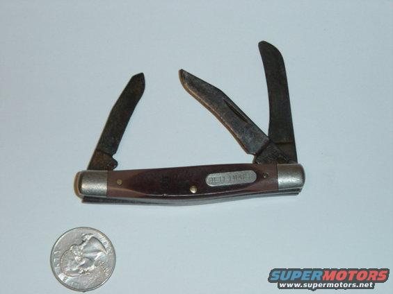 Brown handled pocket knife with three blades open, next to a US quarter