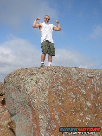 Man flexing on a rock under a blue sky