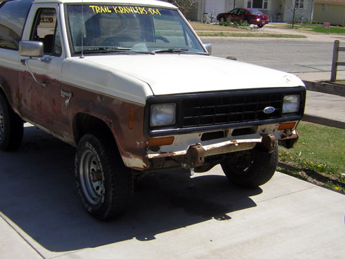 White and brown Ford Bronco II with rust, front view, black grille, missing front bumper section