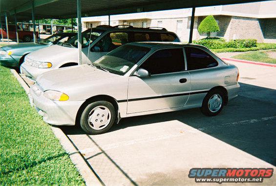 Silver coupe with tinted windows and black trim, parked under a carport next to other vehicles