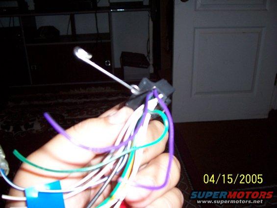 Hand holding a car stereo wiring harness with purple, green, and white wires