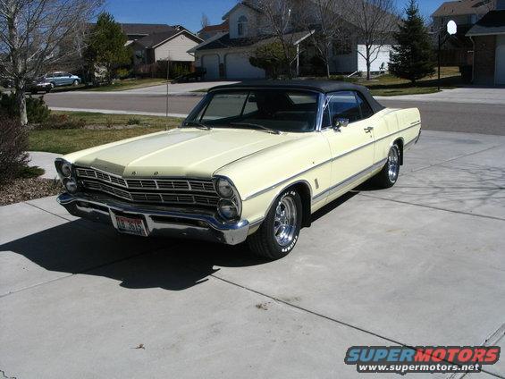 Yellow 1967 Ford Galaxie convertible parked in a driveway. Front grille and headlights are visible