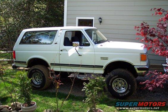 White 1987 Ford Bronco parked in a yard next to a house
