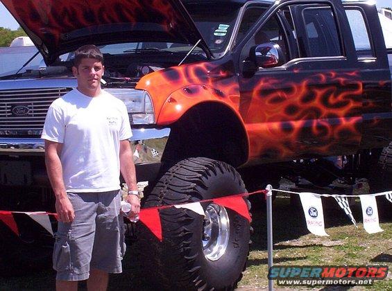 Black lifted truck with orange flame decals, large off-road tires, and an open hood