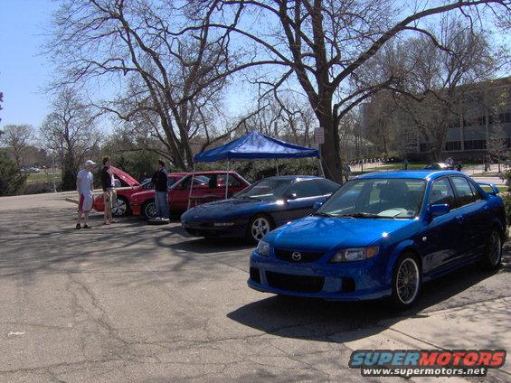 Blue 2003 Mazda Protege sedan parked at car show with other cars behind it
