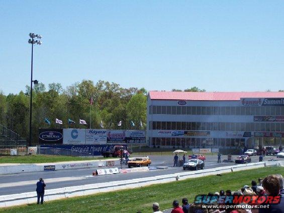 Drag strip scene with cars at the starting line and a grandstand