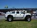 1978 Ford F-250 - A lifted white crew cab pickup truck is parked on grass with grandstands in the background.
