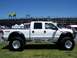 1978 Ford F-250 - A lifted white pickup truck is parked on a grassy area with stadium seating in the background.
