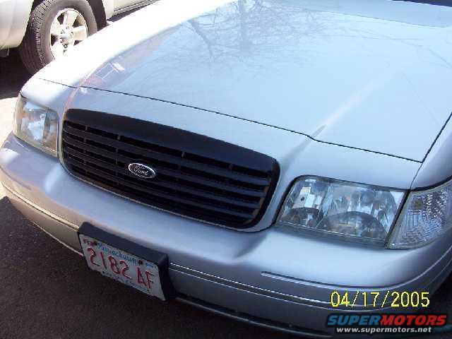 Front of a silver Ford Crown Victoria with a black grille. Another vehicle is partially visible on the left