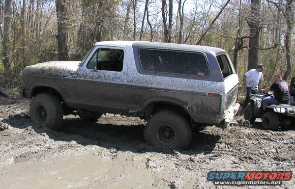 Muddy SUV stuck in a muddy trail with two people on ATVs nearby