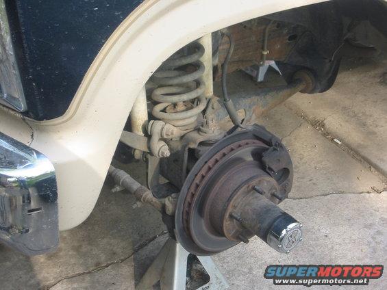 Close-up of a vehicle's front suspension, showing the brake rotor, hub, and coil spring